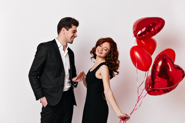 Para celebrująca Walentynki w eleganckich strojach z czerwonymi balonami w kształcie serc